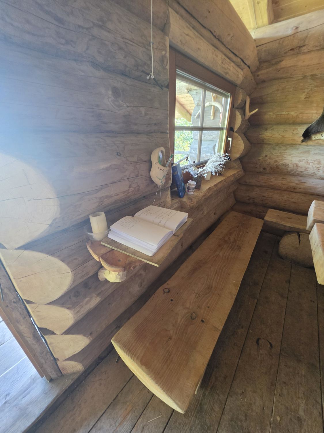 Innenraum der Teufelsfelshütte mit Holzbank, Tisch, Fenster und Hüttenbuch