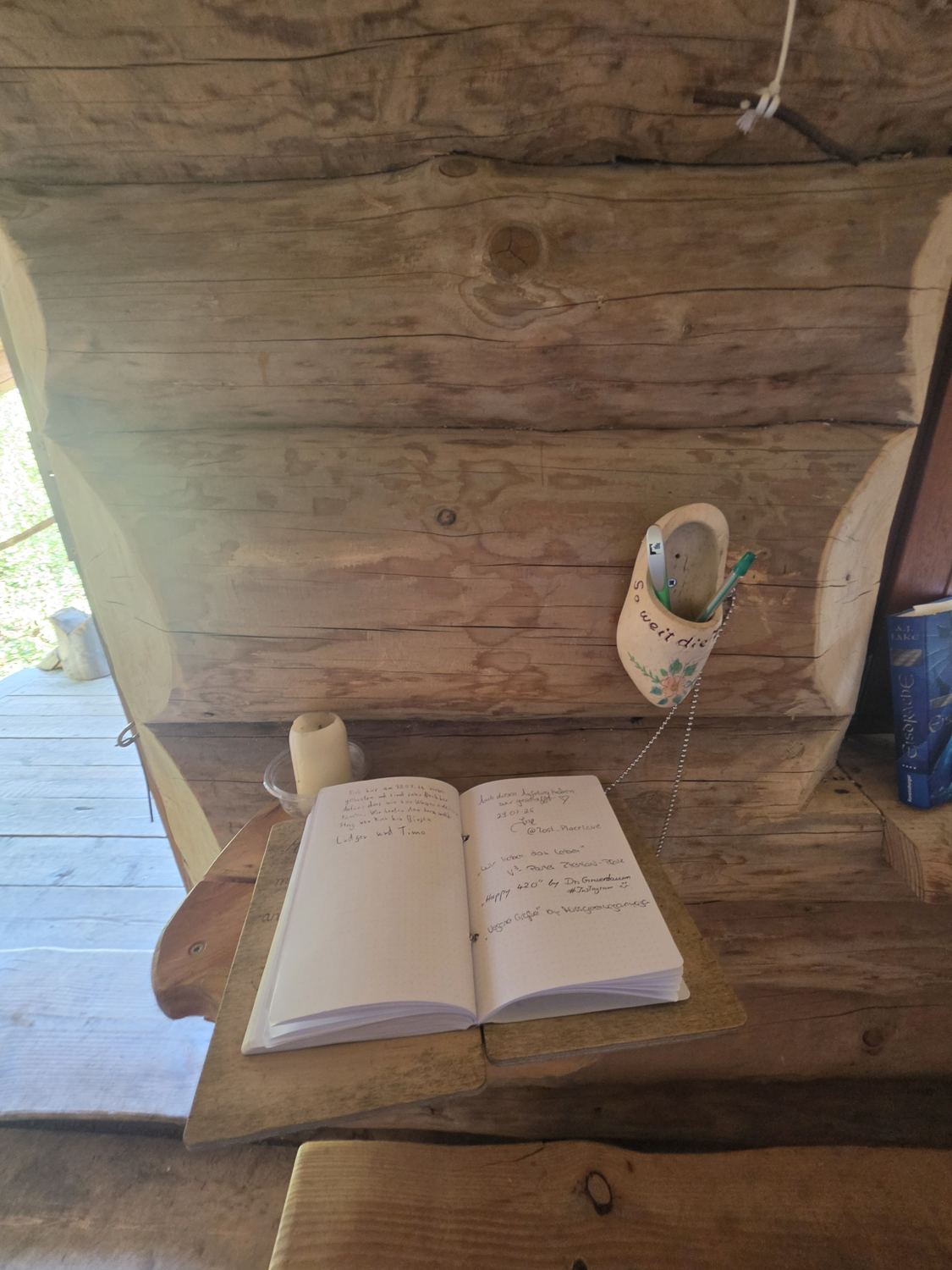 Aufgeschlagenes Hüttenbuch mit handschriftlichen Einträgen, Holzschuh und Kerze